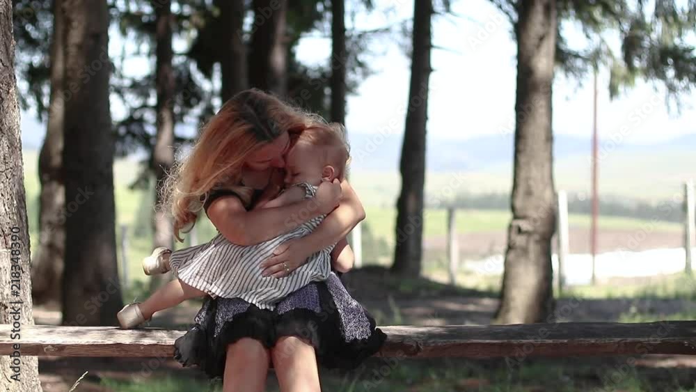 Slow otion mother holding little girl in her arms. Sitting on wood bench in the forest. Parent protecting child Slow otion mother holding little girl in her arms. Sitting on wood bench in the forest. Parent protecting child