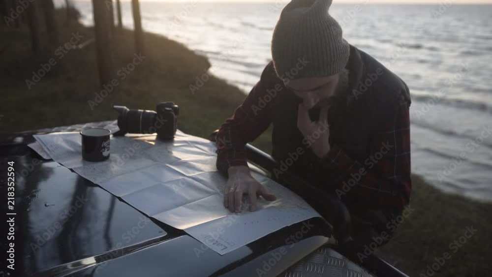 Outdoorsy man with a beard studying map on a bonnet of a vintage 4x4 by the sea, handheld Outdoorsy man with a beard studying map on a bonnet of a vintage 4x4 by the sea, handheld