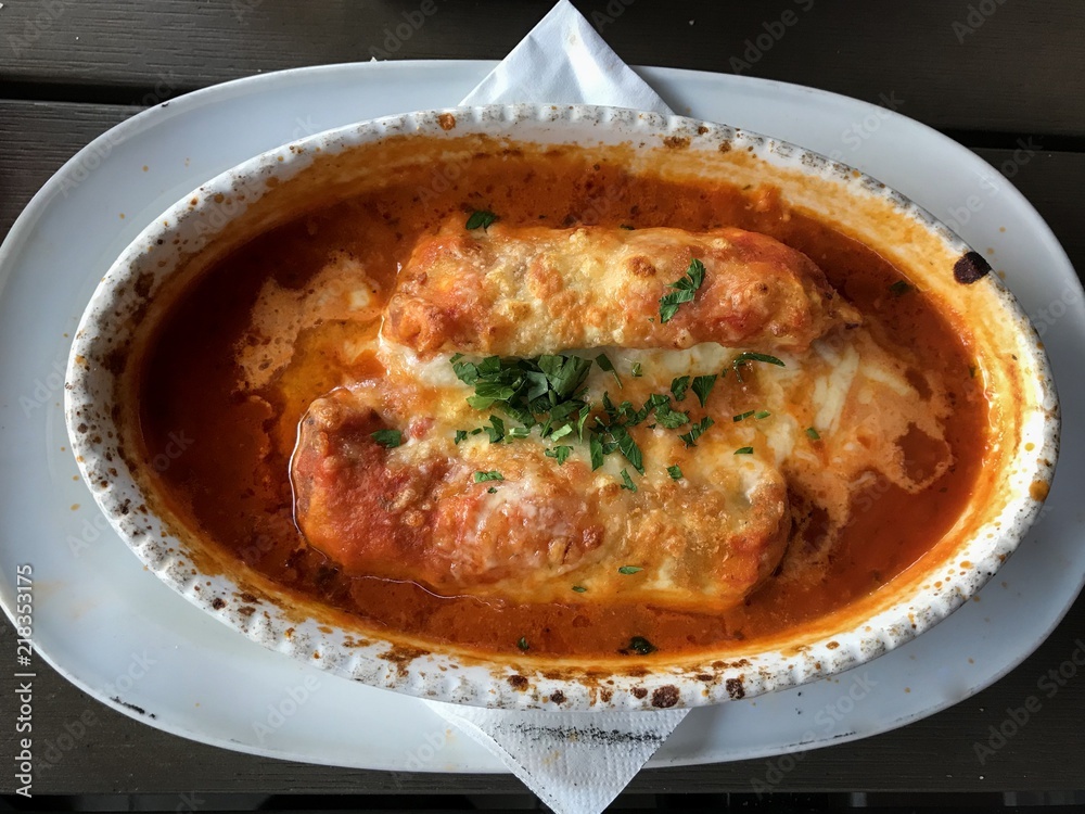 Cannelloni with meat and cheese crust in tomato sauce. Traditional Italian cannelloni. Delicious dinner in an Italian restaurant. Closeup, wallpaper.