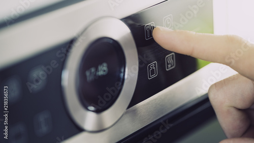 Male finger is touching the button of modern panel of electric oven.