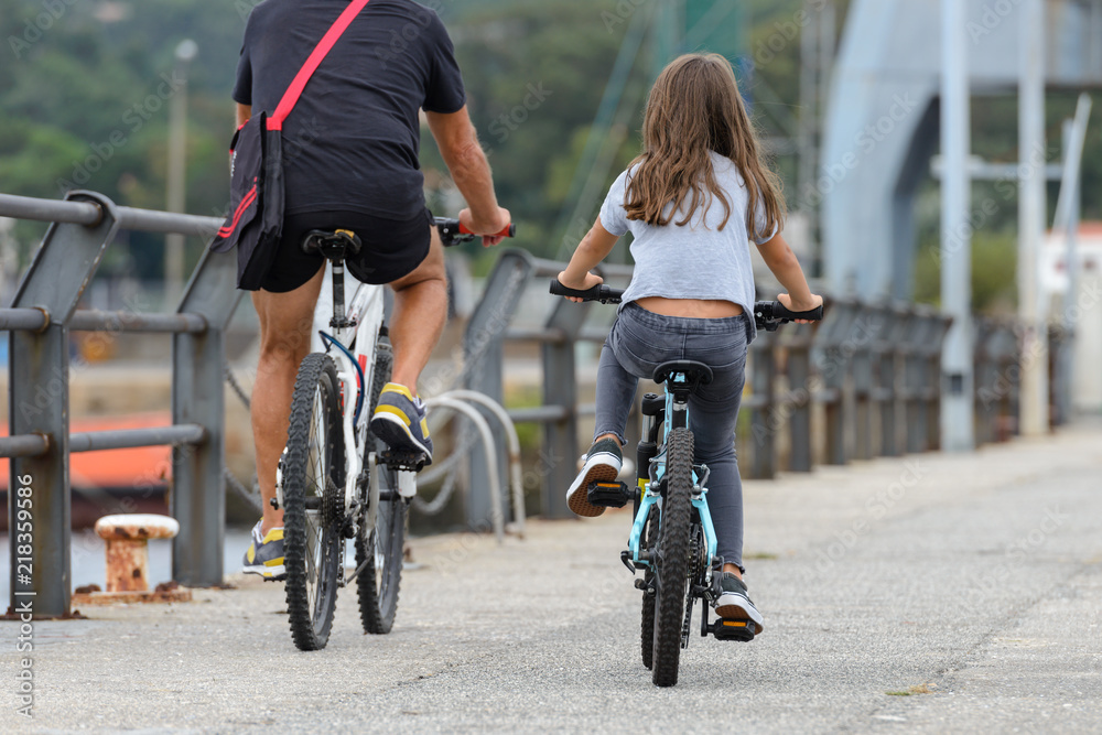 Fototapeta premium father and daughter ride bikes, rear view