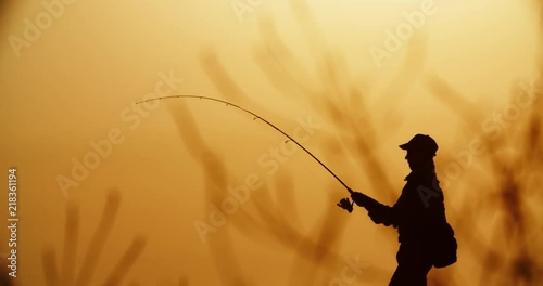 A proficient fishman catching fish with professional spinning rod in hands from the shore. lake in golden sunset 4k