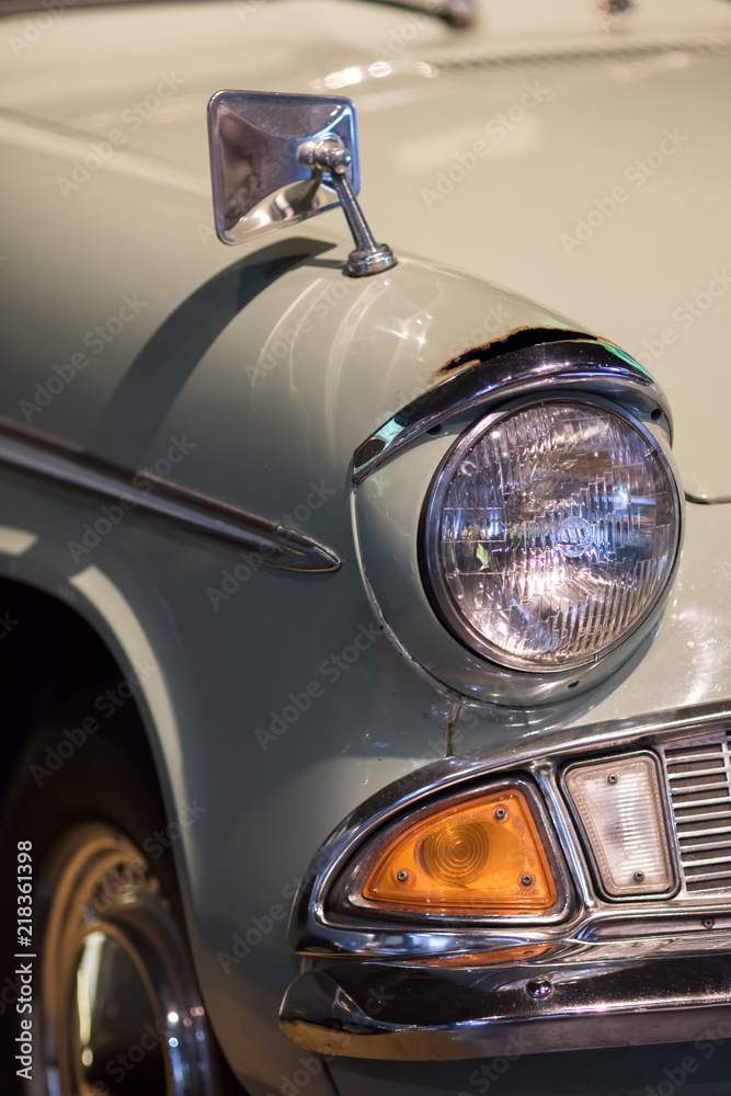 Vintage restored classic car close-up. Sealed-beam retro headlamp. Sixties headlight and wing mirror on old rusty collectors automobile.