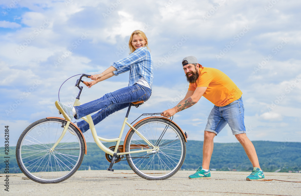 Fototapeta premium Woman rides bicycle sky background. Man helps keep balance and ride bike. How to learn to ride bike as adult. Girl cycling while boyfriend support her. Cycling technique. Learn cycling with support