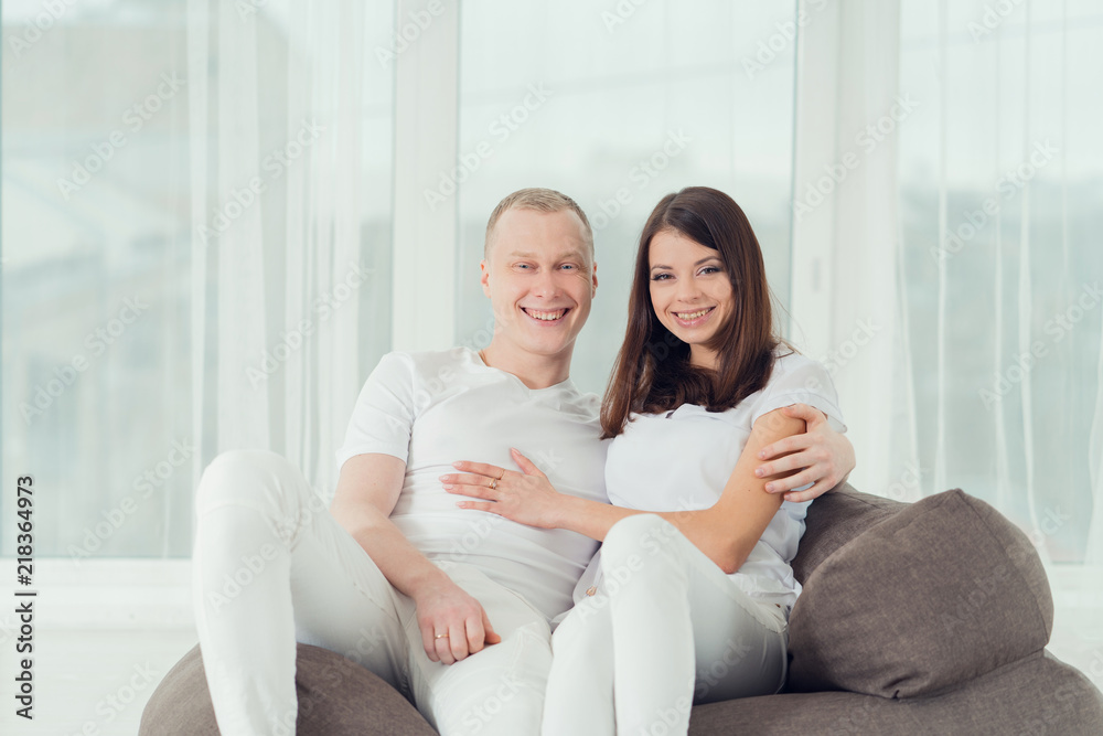 young happy couple in white clothes sitting in armchair, smiling