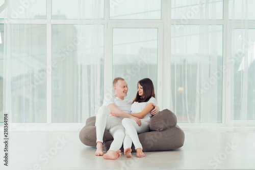 young happy couple in white clothes sitting in armchair, smiling