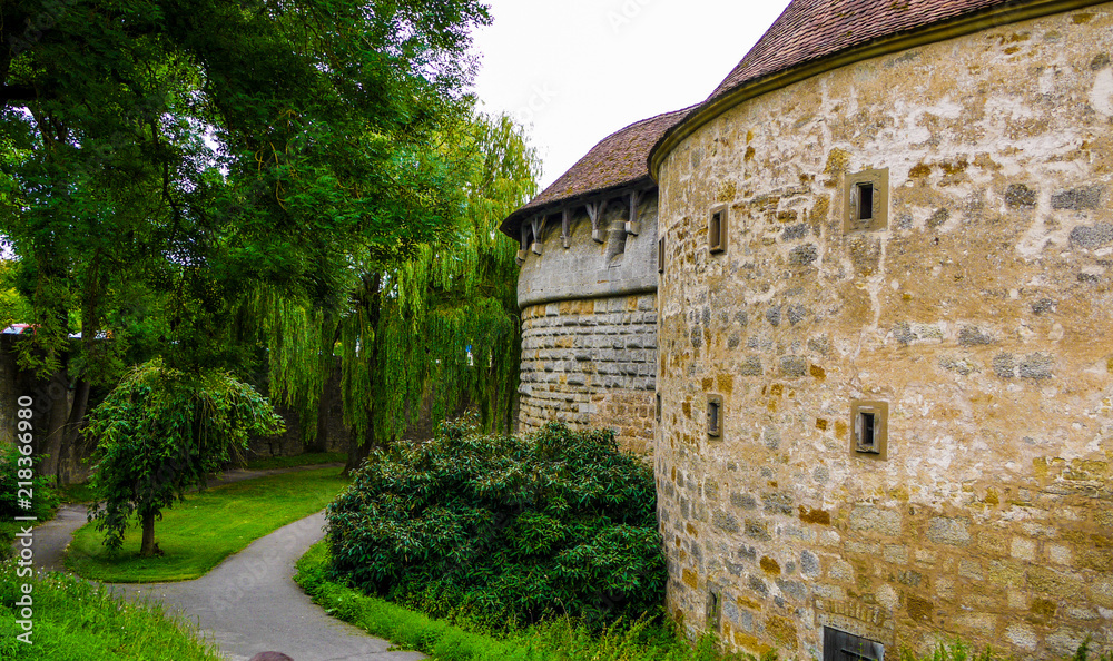 Old stone wall of part of a fortified castle with surrounding trees and a timber roof. Taken in Rothenburg Ob Der Tauber, Germany on a cloudy day.