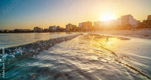 Wavy curves of sea is covered in golden sunset light. Sea at sunset sunlight. Wavy curves pattern on beach. Waves in bokeh focud