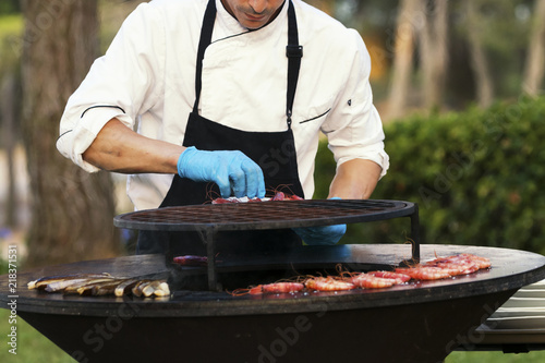 Chief cooking shrimps on grill outdoor.