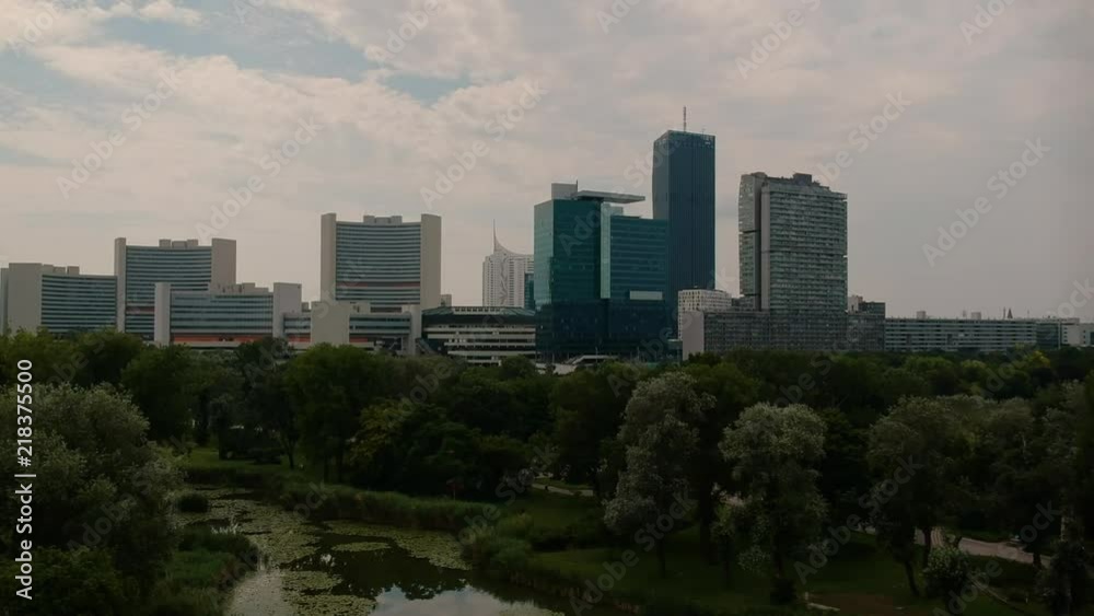 Donaucity skyline push-in shot behind green park with pond AERIAL Donaucity skyline push-in shot behind green park with pond AERIAL