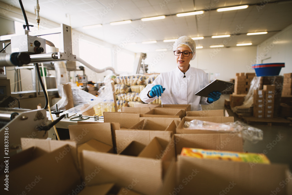 Young female worker in sterile clothes is using tablet to check right number of packages. Young female worker in sterile clothes is using tablet to check right number of packages.