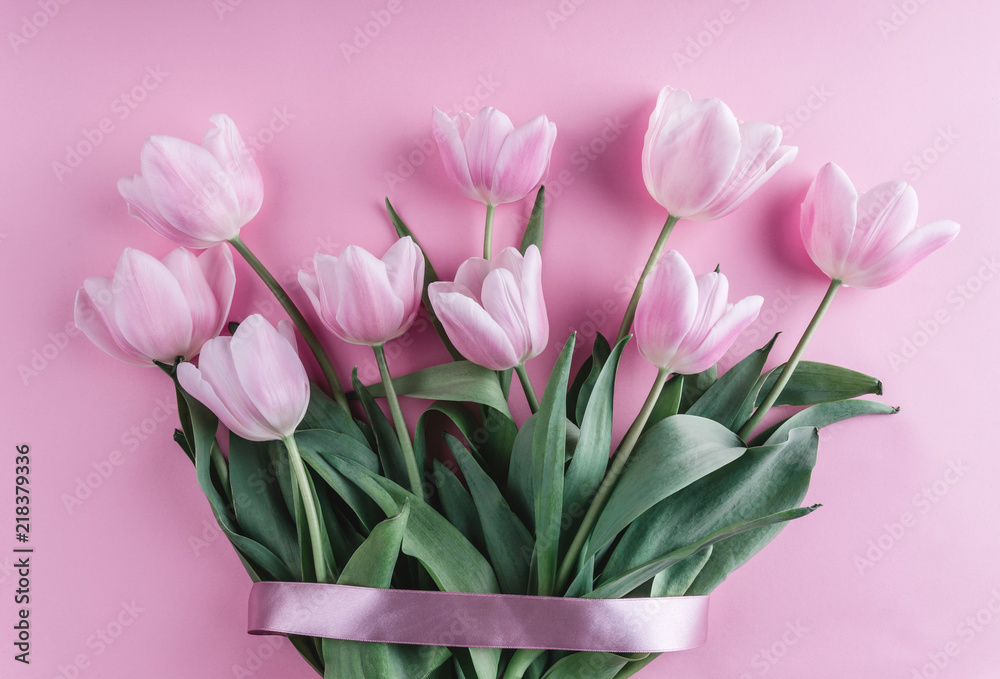 Fototapeta premium Bouquet of pink tulips flowers over light pink background. Greeting card or wedding invitation. Flat lay, top view, copy space.