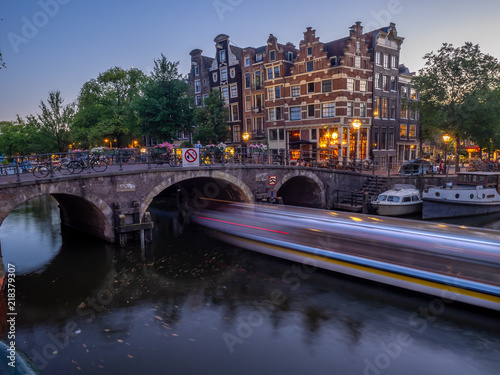 Amsterdam canal, bridge and typical houses, boats and bicycles during evening twilight blue hour, Holland, Netherlands.