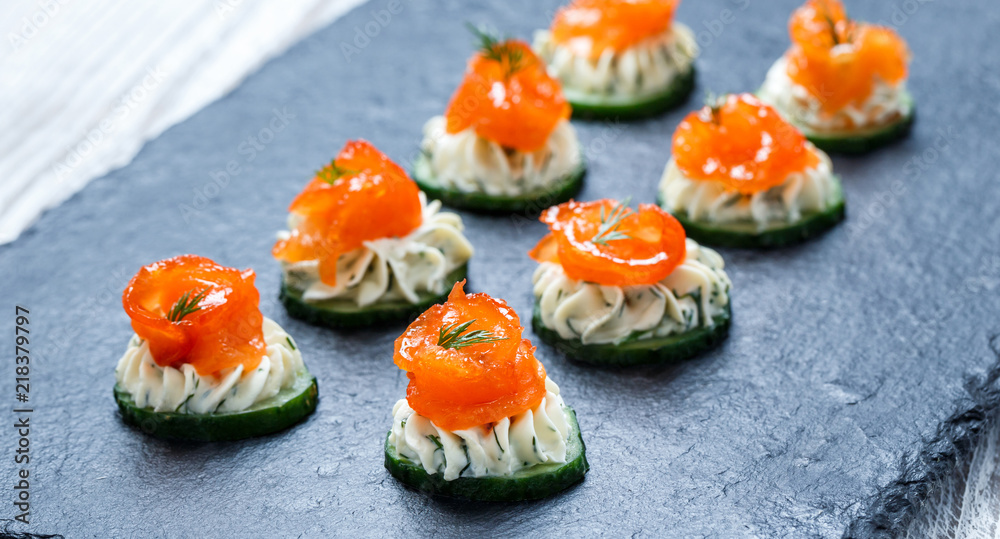 Appetizer canape with salmon, cucumber and cream cheese on stone slate background close up. Delicious snacks, sandwiches