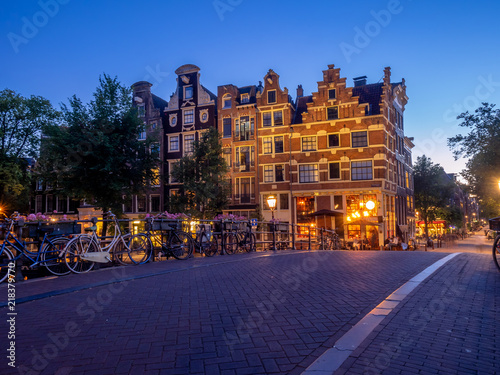 Amsterdam canal, bridge and typical houses, boats and bicycles during evening twilight blue hour, Holland, Netherlands.