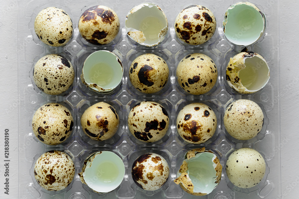 Quail eggs in a transparent plastic container on gray wooden background. Top view.
