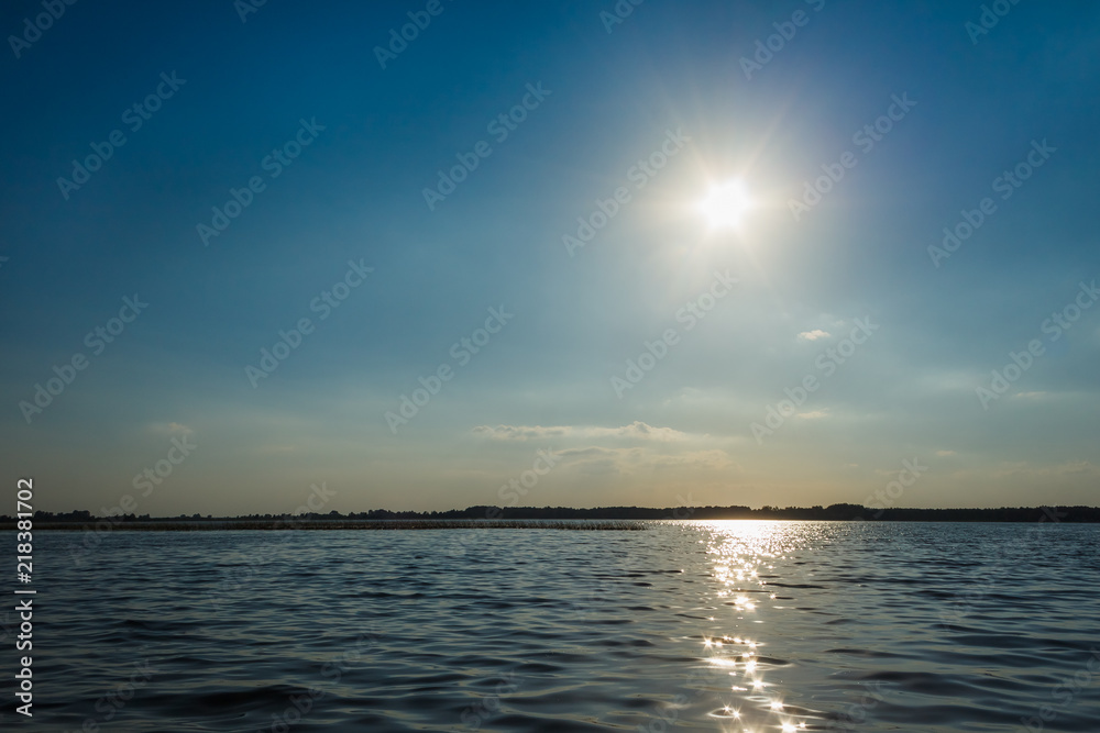 Waves and glare on the surface of the water. Lake on a sunny day with blue sky and white clouds