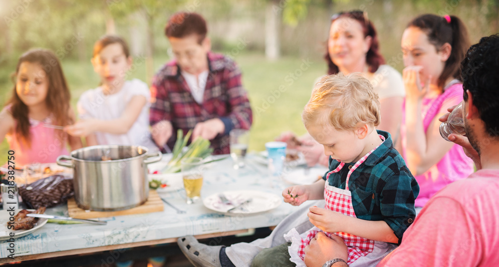 Big happy family is sitting at the picnic table and enjoying food on a sunny day.