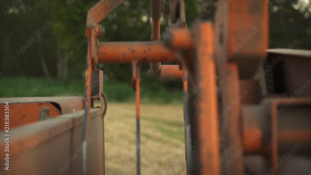 Close-Up of the Hay Bale Press running while the farmer walks by in the background with his rake. Close-Up of the Hay Bale Press running while the farmer walks by in the background with his rake.