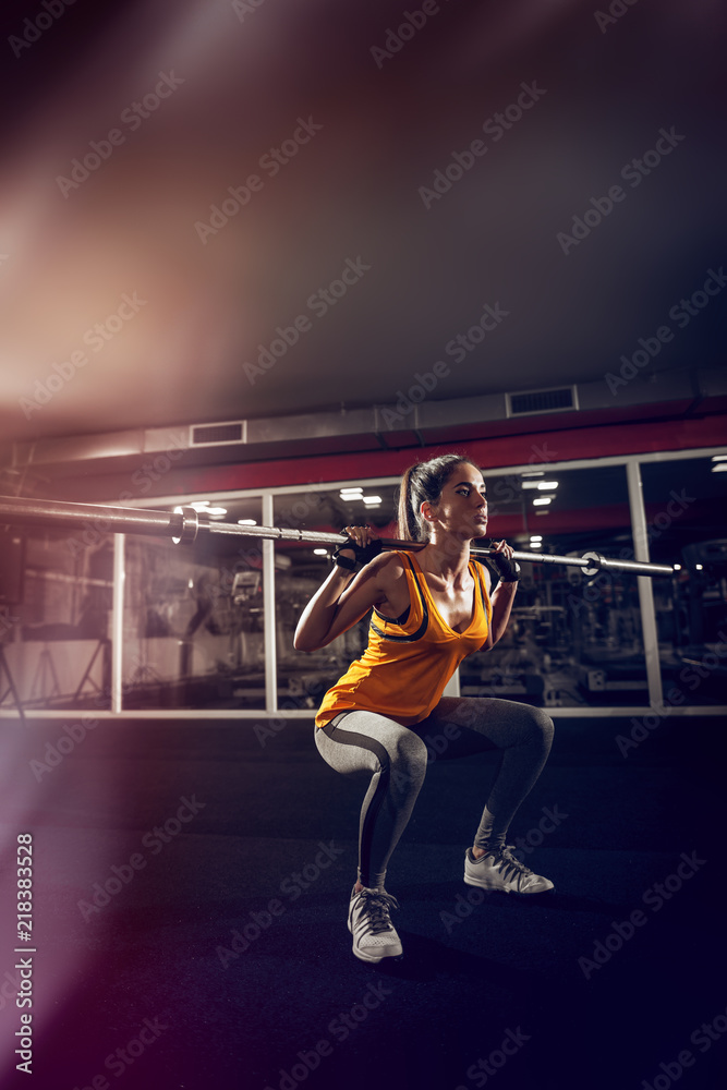 Close up of a young strong fitness female model doing squats with weight.