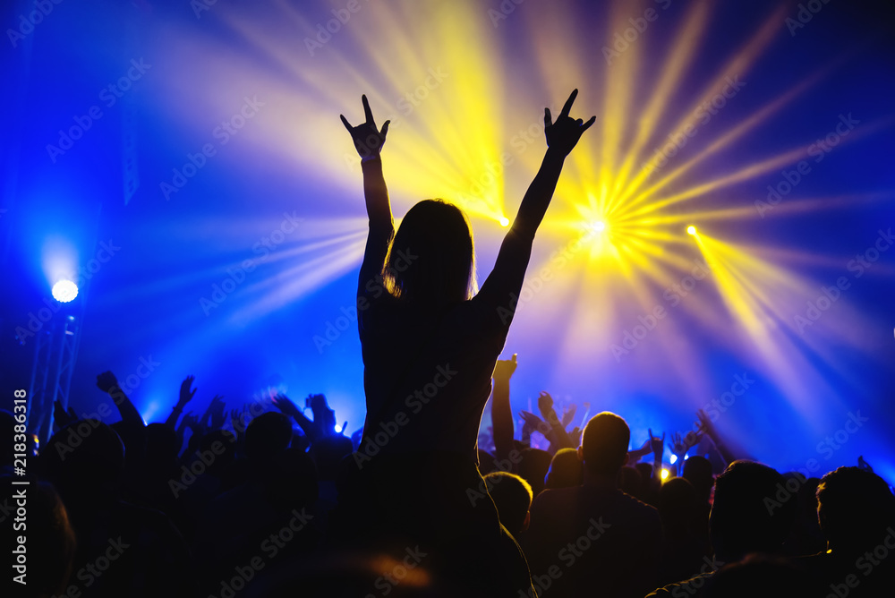 The girl shows the sign of the horn during a concert of a rock band at the club. A crowd of people during the concert. A hand with two fingers. Silhouette at the concert.
