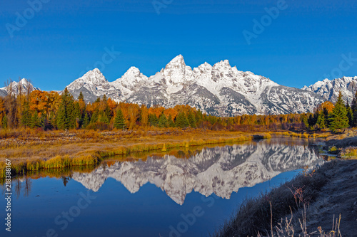 Snow covered grand tetons range reflected in the calm water with vibrant fall foliage in the foreground © Sekar B