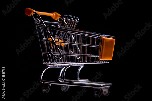 Miniature metal shopping cart with orange elements shot against a black background