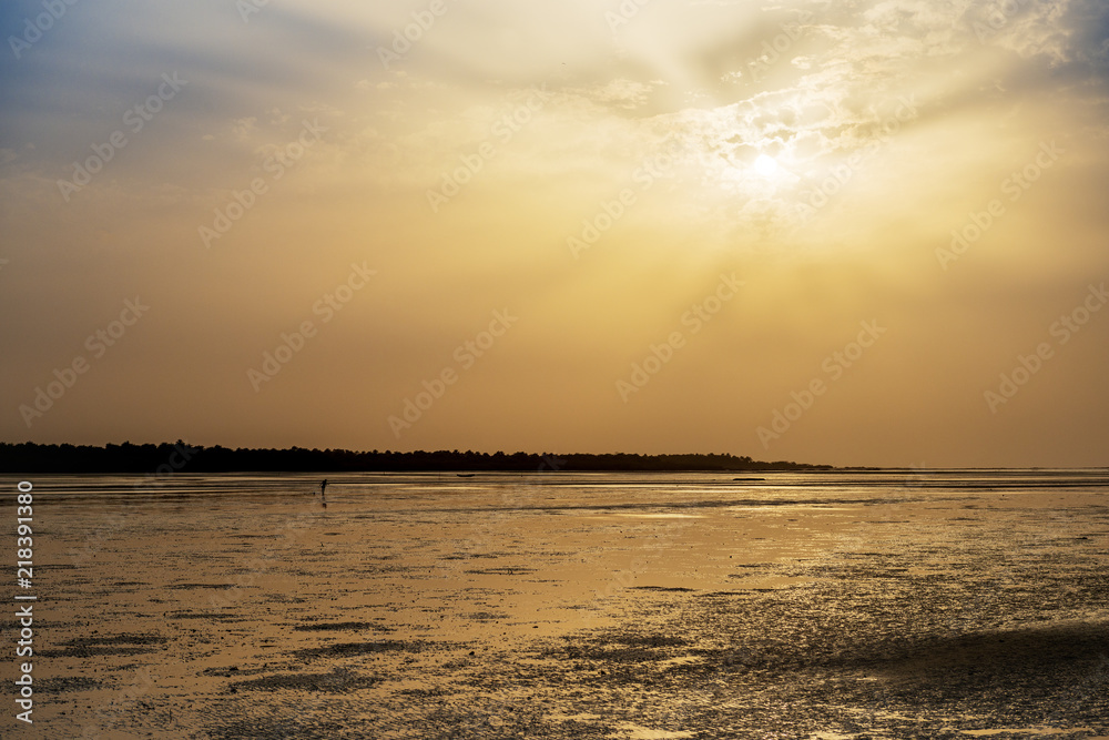 Obraz premium Silhouette of a cockle catcher at the beach in the island of Orango at sunset, in Guinea Bissau. Orango is part of the Bijagos Archipelago; Concept for travel in Africa and summer vacations