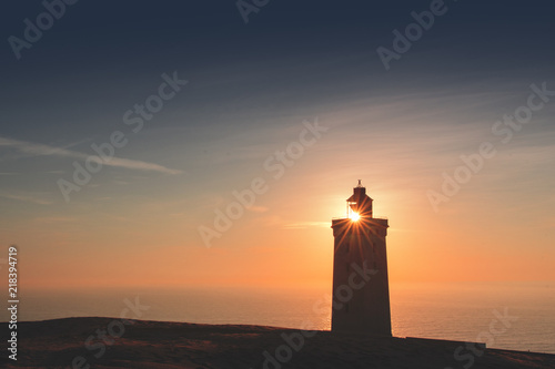 Silhouette of a lighthouse with lens flare and sand dunes in sunset light. Rubjerg Knude Lighthouse, Lønstrup in North Jutland in Denmark, Skagerrak, North Sea