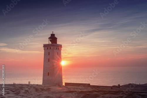 Lighthouse landmark with lens flare and sun star in evening sunset light. Endless sun dunes. Rubjerg Knude Lighthouse, Lønstrup in North Jutland in Denmark, Skagerrak, North Sea