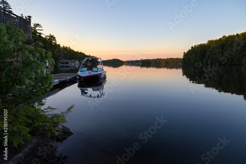 A boathouse with a wakeboard boat parked at it on Lake Joseph at dawn. photo