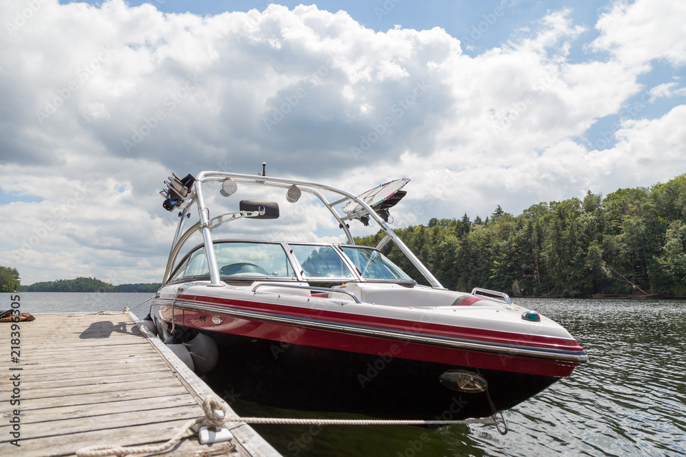 A wakeboard boat at a wooden dock in the Muskokas on a sunny day. - obrazy, fototapety, plakaty 