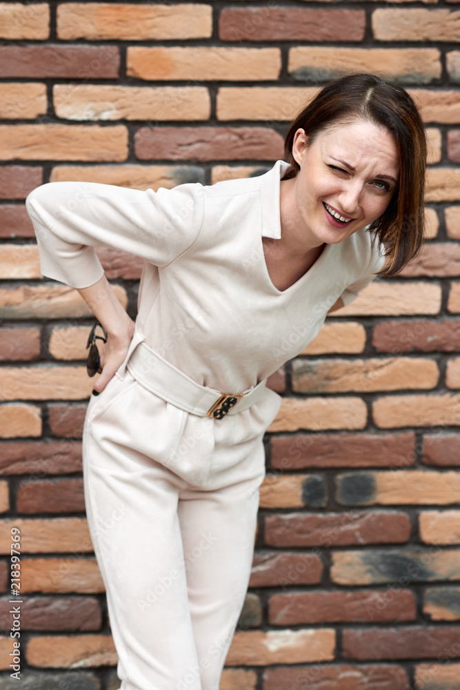 girl standing by a brick wall and has a back pain girl standing by a brick wall and has a back pain
