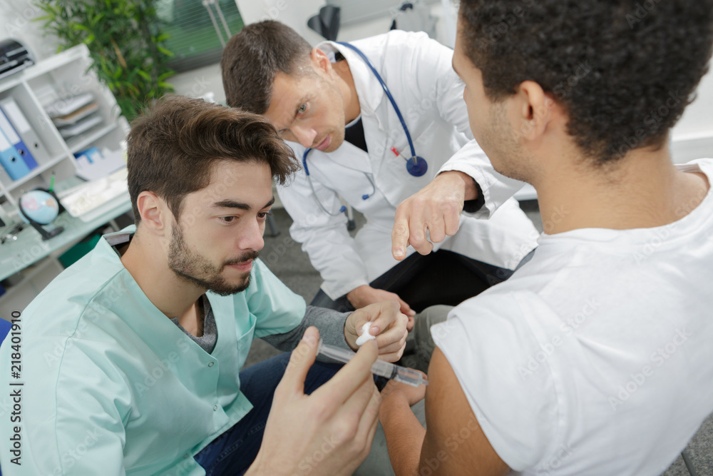 Fototapeta premium handsome intenrist injecting patient under mature doctors surveillance