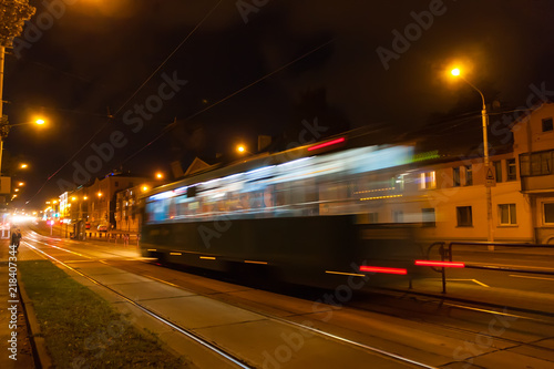 The motion of a blurred tram down the street in the evening.