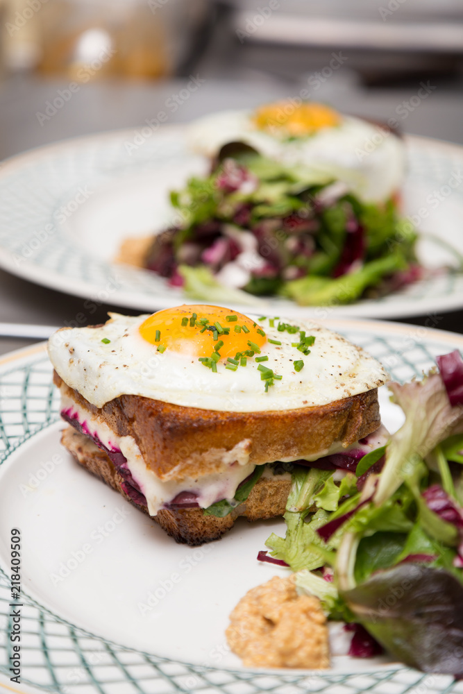 A sandwich with a side of salad and an egg on-top.
