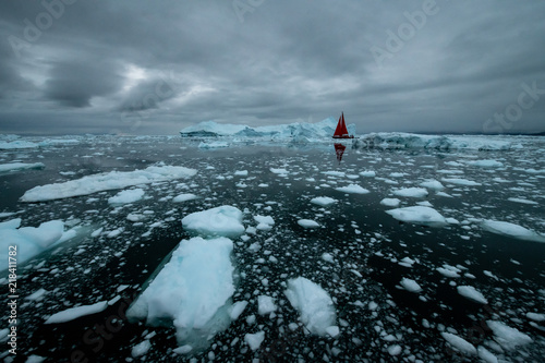Greenland iceberg mirror panorama with red sail ship and heavy clouds 