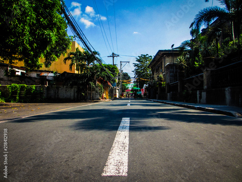 Perspective shot of a Manila city street road with trees and brightly painted buildings on a summer day