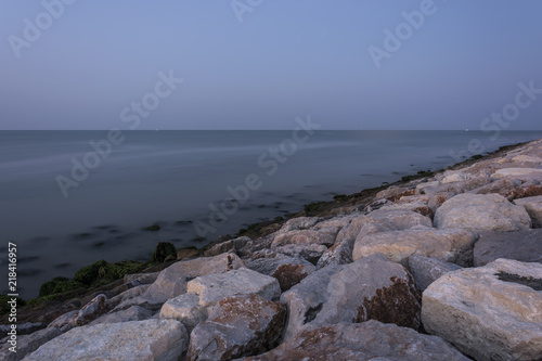 The infinity horizon above the sea. The stone beach with moss and eyelashes. The waves flow to the coastline. Morning atmosphere before sunrise.