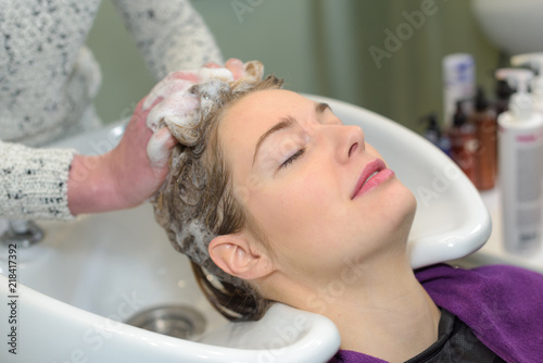 happy young woman with hairdresser washing head at hair salon