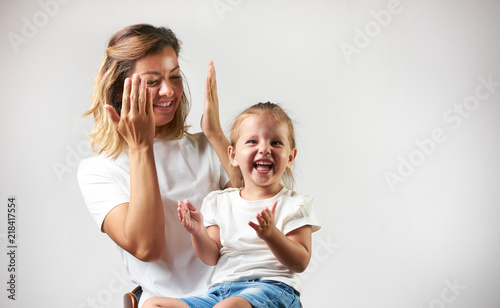 Fotografie Little girl playing peekaboo game with her mother on white background with copy space