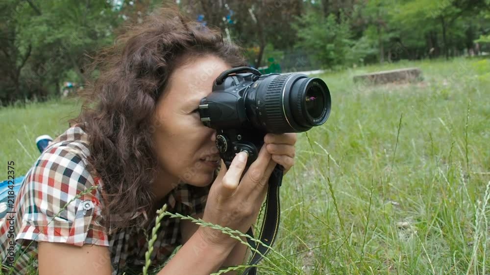 A woman photographer at work. Woman with photo camera lying down in grass. A woman photographer at work. Woman with photo camera lying down in grass.