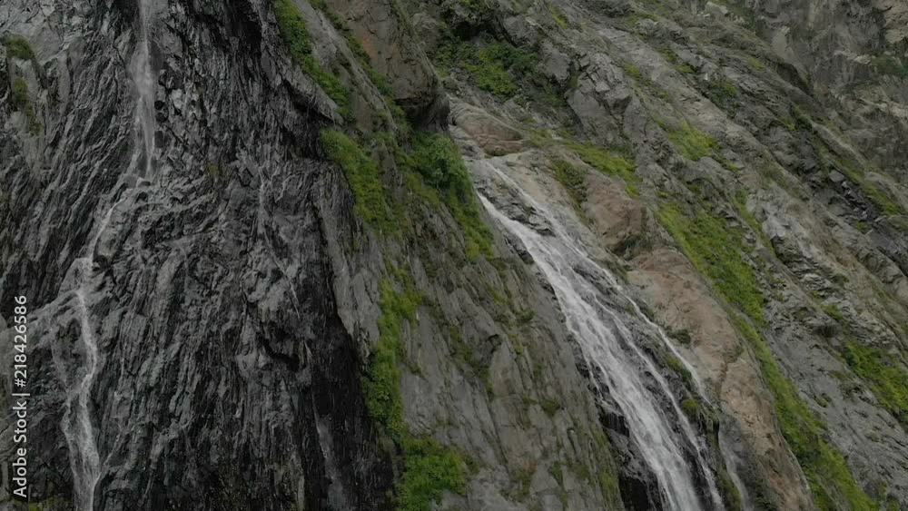 Tracking and top shot Air shot from a stream of water splashing waterfall on a rock wall in the Caucasus Mountains. Around the jet of the waterfall Tracking and top shot Air shot from a stream of water splashing waterfall on a rock wall in the Caucasus Mountains. Around the jet of the waterfall