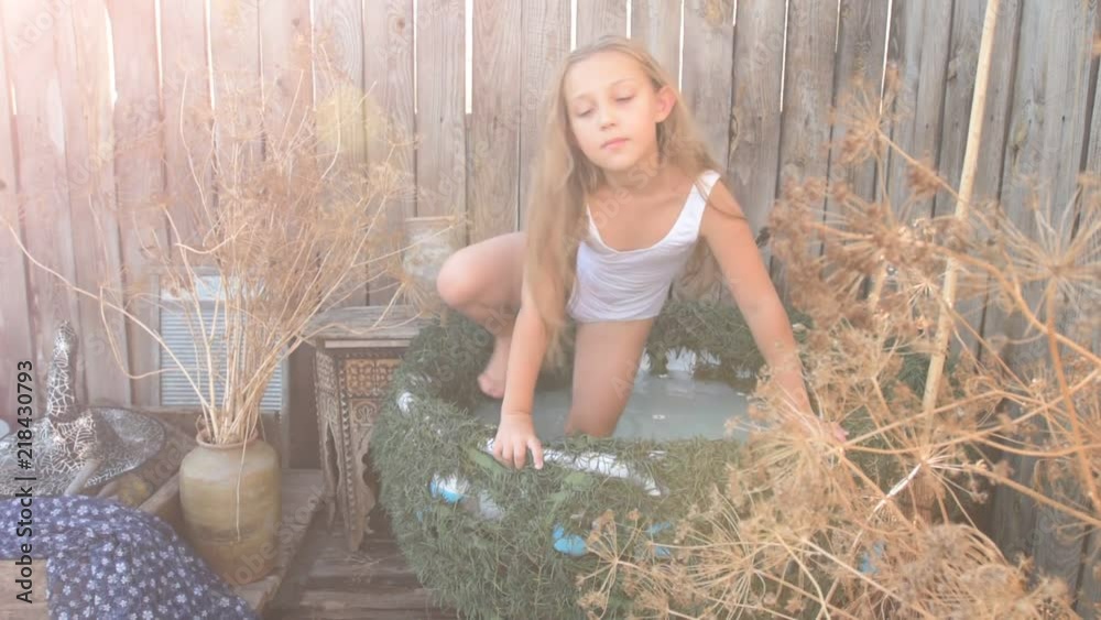 Young girl is preparing to take part in celebration of Halloween. Child is bathing in cauldron with chamomile flowers, trying on pointed hat. She is ready to fly on broomstick like a witch.