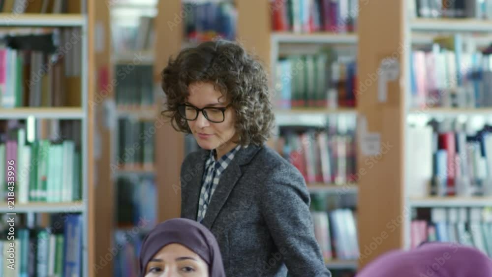 Caucasian female teacher smiling and talking with cheerful woman in hijab while giving a lesson for migrants in language school Caucasian female teacher smiling and talking with cheerful woman in hijab while giving a lesson for migrants in language school