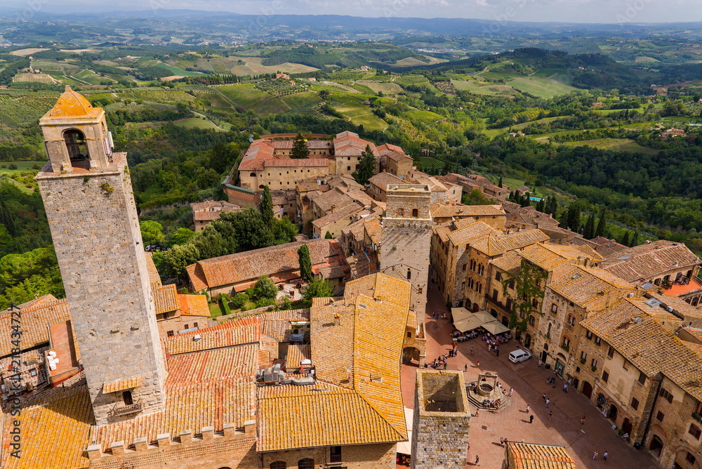 Top aerial panoramic view of medieval old town in San Gimignano, Tuscany region, Italy. View from the tower located among old Tuscany house and tower surround by field, meadows and vineyards.