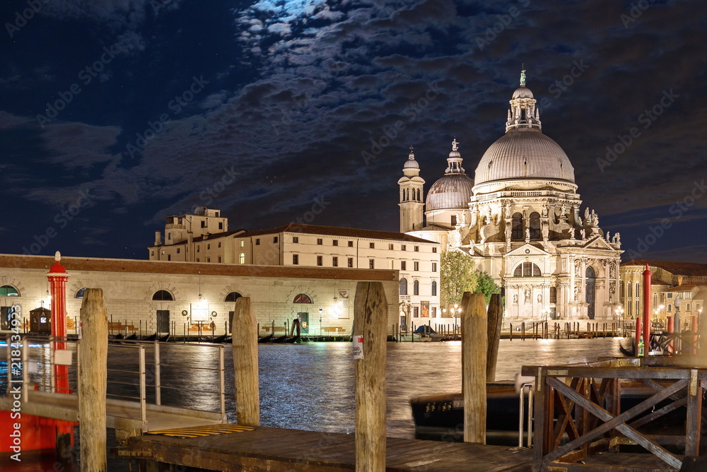 Night view of grand canal and its riverside and pier, Venetian Gothic architectures and background of Basilica di Santa Maria della Salute in Venice, Italy