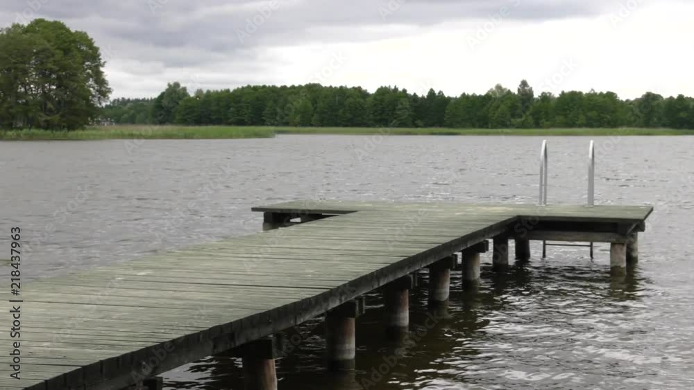 A wooden bridge over the lake. Grass and reeds in the background. Gentle waves. A wooden bridge over the lake. Grass and reeds in the background. Gentle waves.