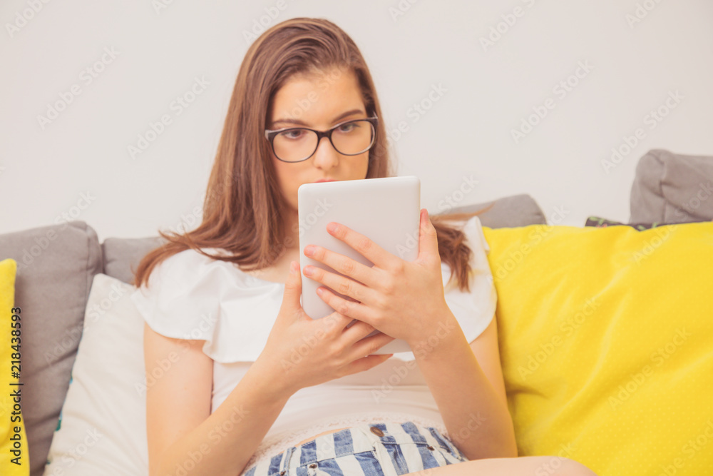 Cute teenager girl using digital tablet while sitting on the couch at home.