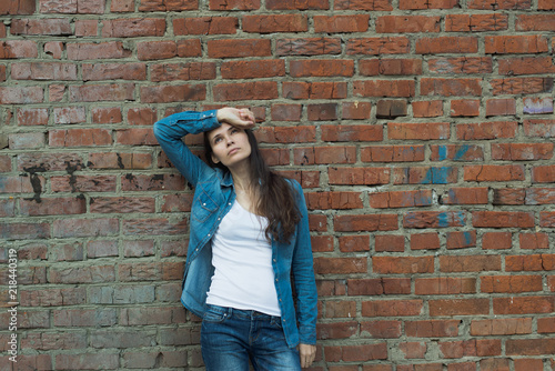 adult girl standing in denim clothing and white t-shirt and sad looking up on red brick wall background with copy space, stock photo image
